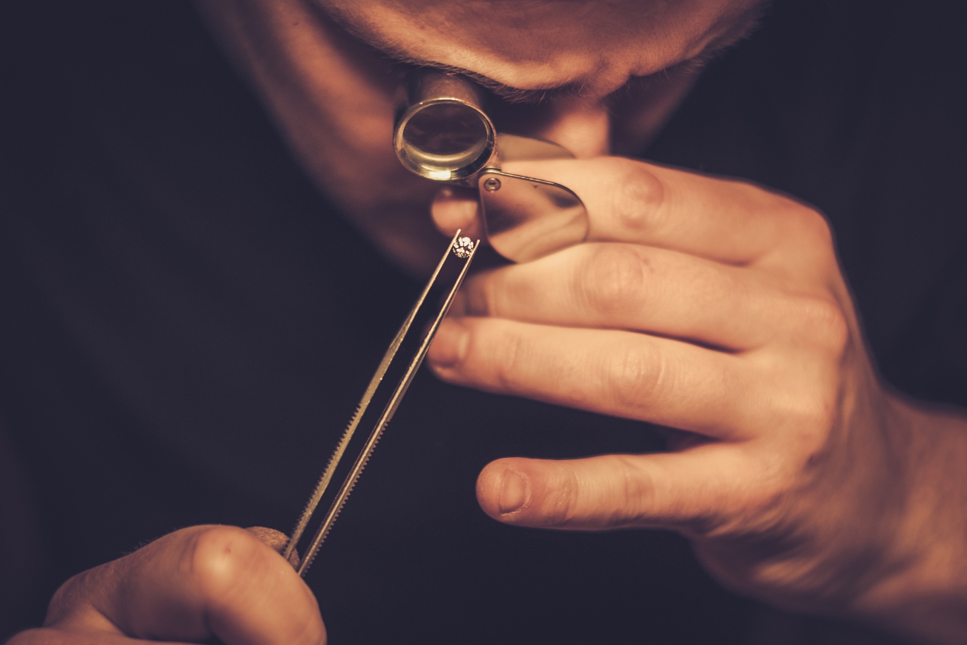 Un bijoutier observe un diamant tenu par une pince avec une loupe